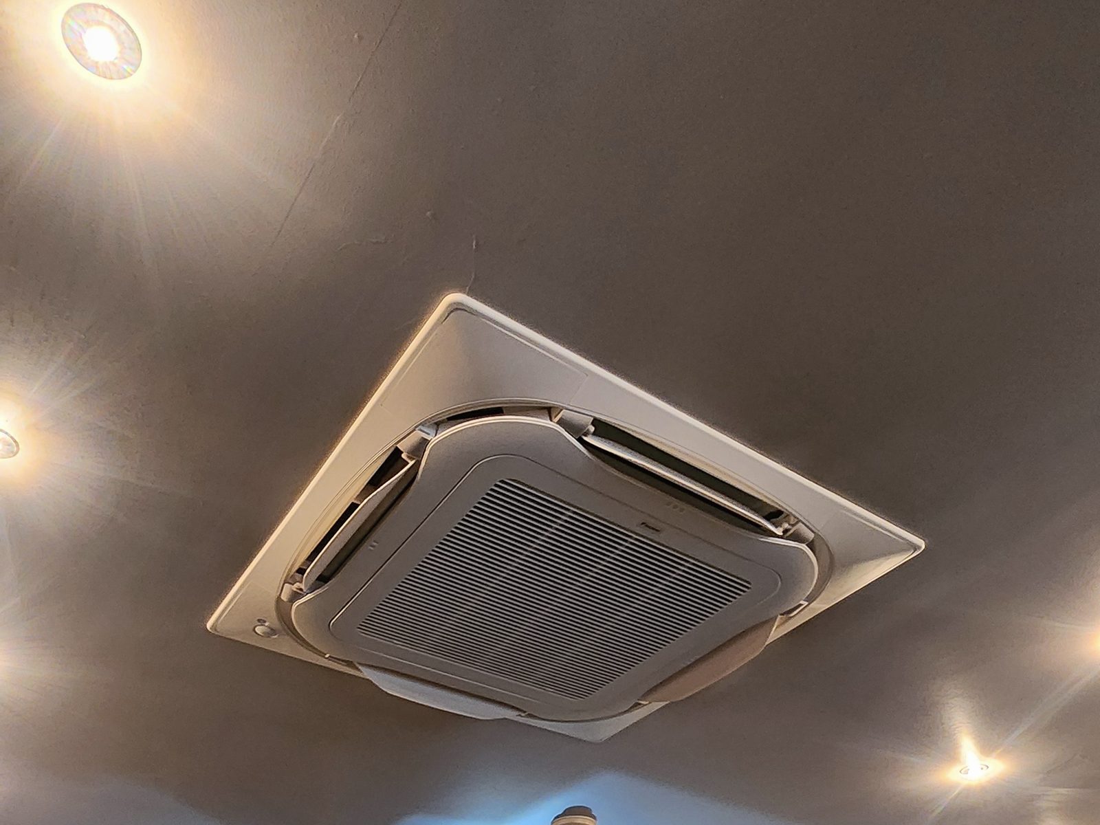 A ceiling cassette air-conditioning unit in a commercial ceiling with recessed downlights.