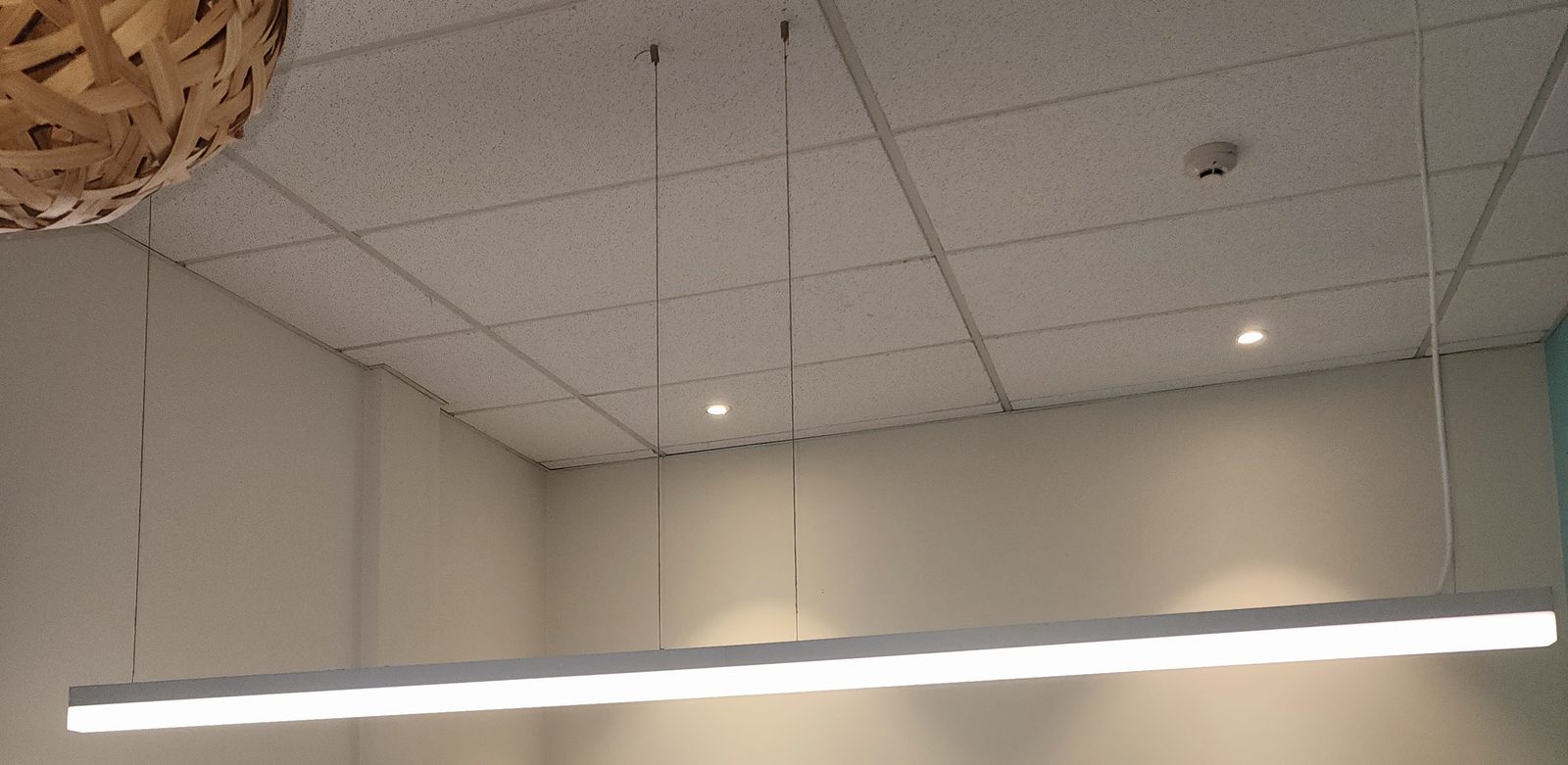 A suspended linear LED light under a grid ceiling.