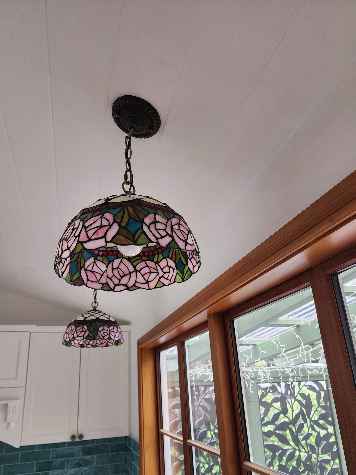 Two leadlight glass pendant lights hung from a white panelled ceiling beside timber-framed windows.