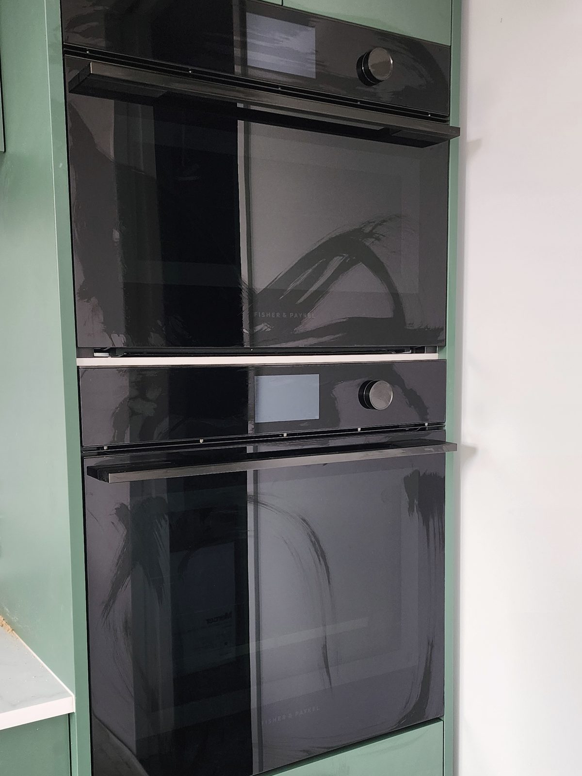 Two black built-in wall ovens stacked in green kitchen cabinetry.