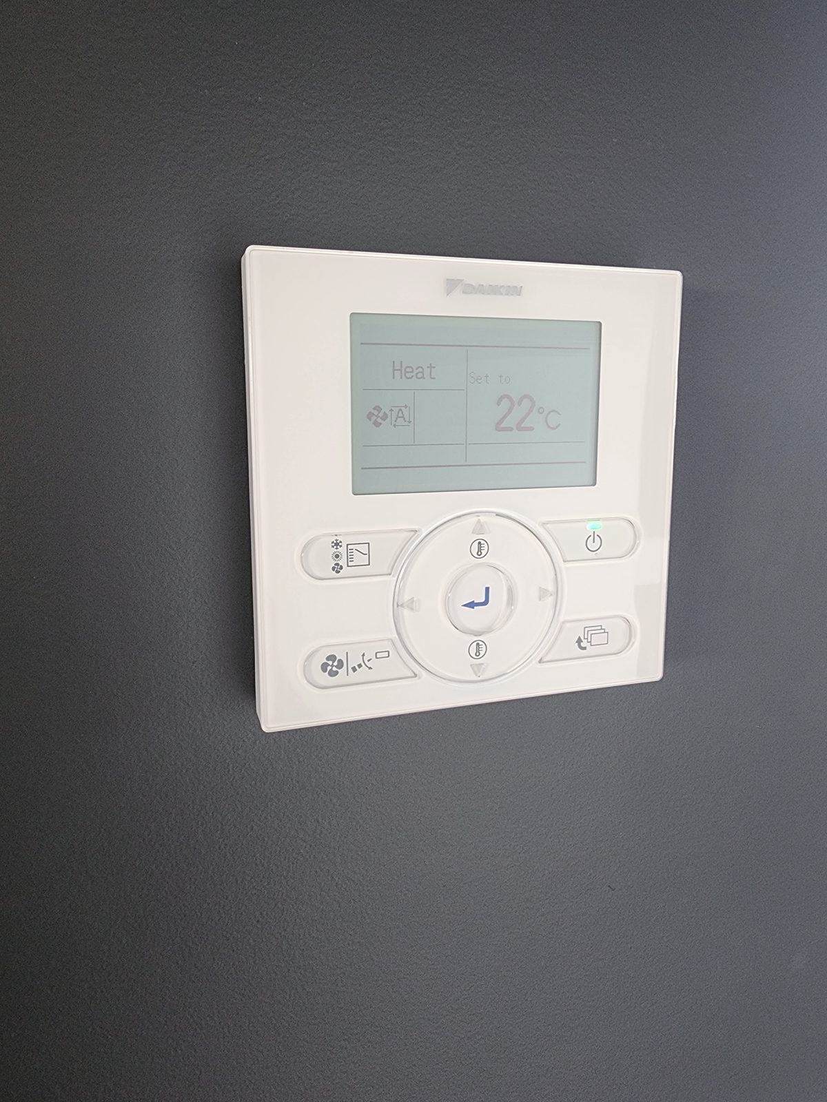 A Daikin wall controller on a dark wall, its screen showing Heat mode set to 22 degrees.