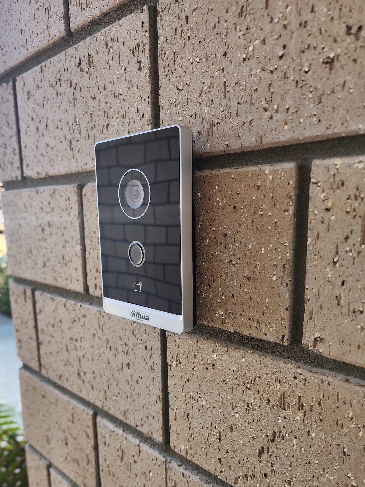 A Dahua video door station with a camera, call button and card reader on a brick wall.