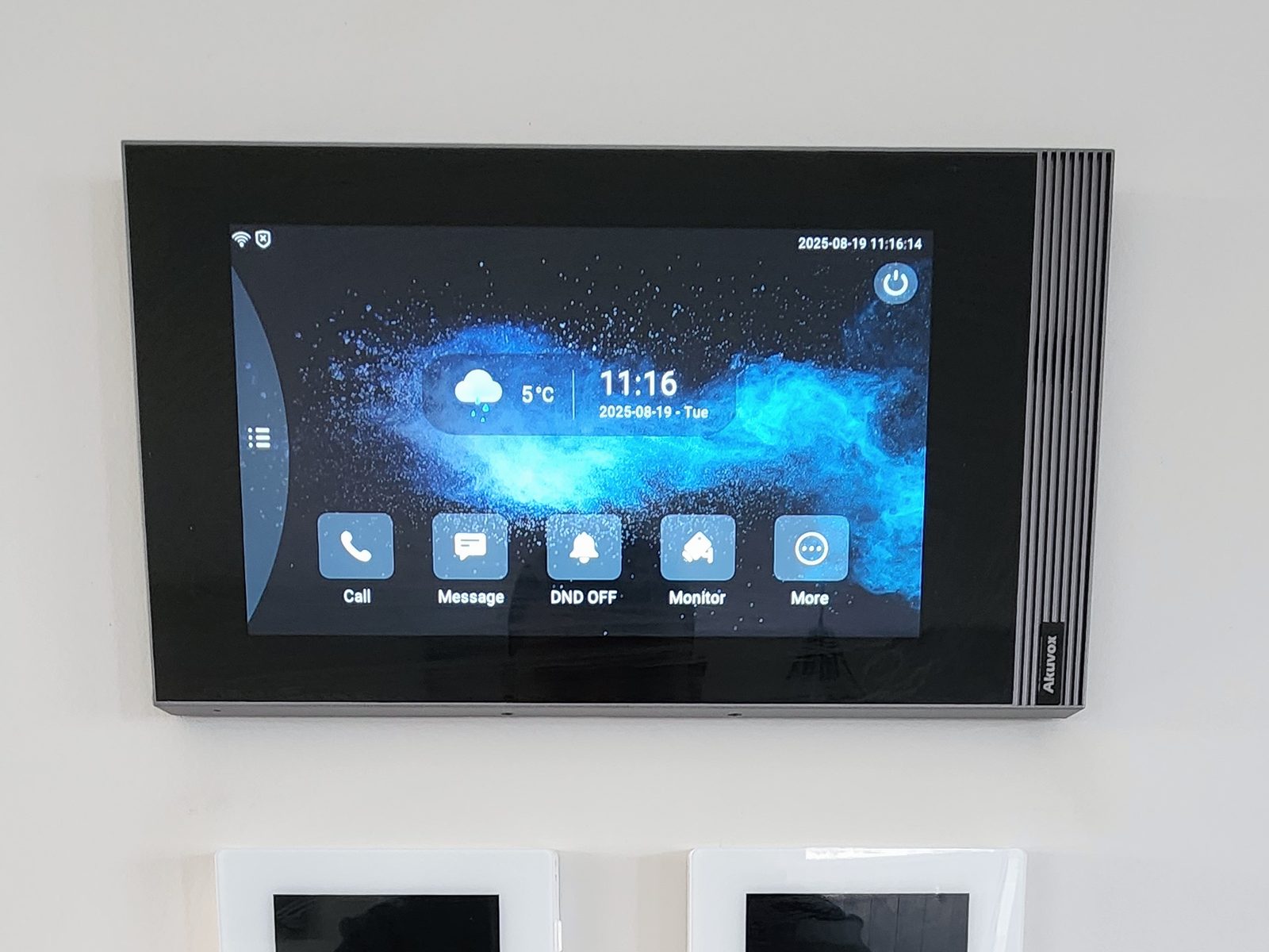 A wall-mounted Akuvox intercom touch screen above three dark glass touch panels and a white switch plate.