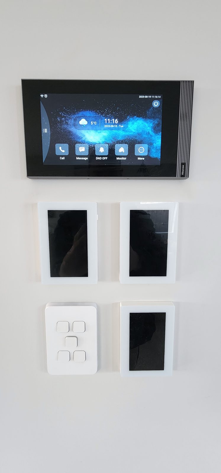 A wall-mounted Akuvox intercom touch screen above three dark glass touch panels and a white switch plate.