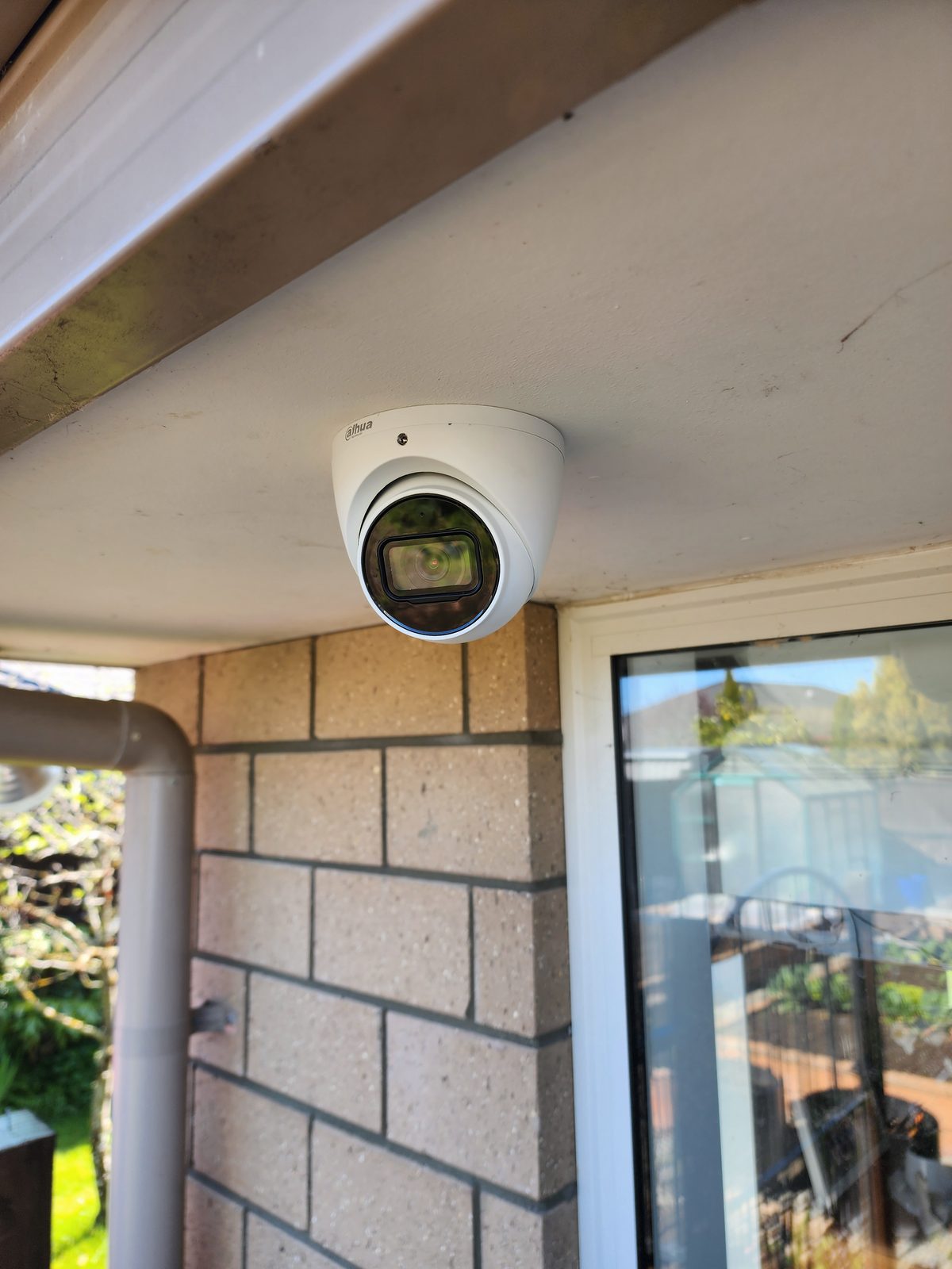 A white Dahua turret security camera mounted under the soffit of a brick house.